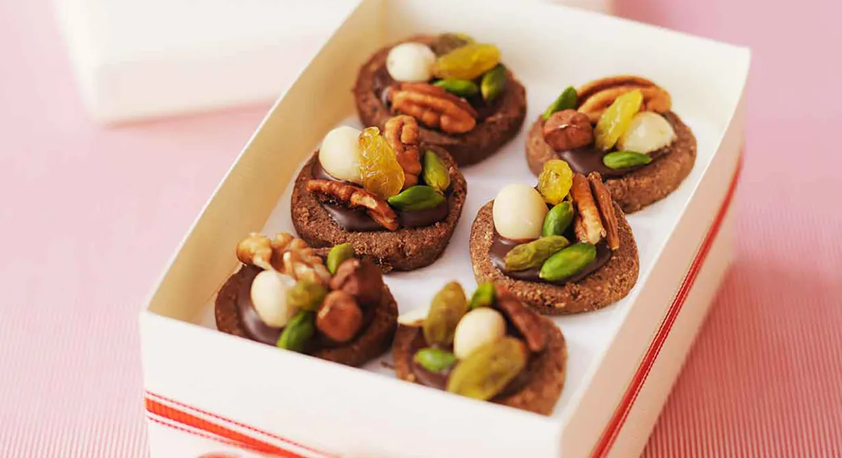 Som små praliner blir de här choklad- och nötkakorna när de garneras med choklad, nötter och russin. Fina småkakor att packa in i cellofan och placera väl synliga på disken.